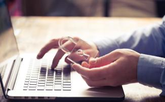 Hands working on laptop, one hand holding glass lock